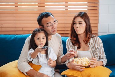 Ebeveynlerden oluşan Asyalı bir aile, evde oturma odasındaki kanepede patlamış mısır yiyen mutlu bir kız ya da televizyon izleyen bir film. Rahatlatıcı mutluluğun tadını çıkar.