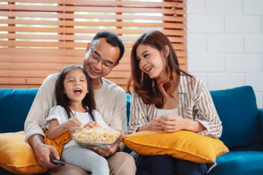 Ebeveynlerden oluşan Asyalı bir aile, evde oturma odasındaki kanepede patlamış mısır yiyen mutlu bir kız ya da televizyon izleyen bir film. Rahatlatıcı mutluluğun tadını çıkar.