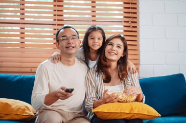 Ebeveynlerden oluşan Asyalı bir aile, evde oturma odasındaki kanepede patlamış mısır yiyen mutlu bir kız ya da televizyon izleyen bir film. Rahatlatıcı mutluluğun tadını çıkar.