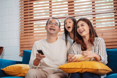 Ebeveynlerden oluşan Asyalı bir aile, evde oturma odasındaki kanepede patlamış mısır yiyen mutlu bir kız ya da televizyon izleyen bir film. Rahatlatıcı mutluluğun tadını çıkar.