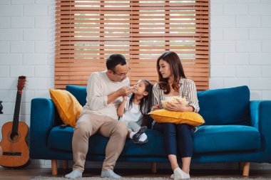 Ebeveynlerden oluşan Asyalı bir aile, evde oturma odasındaki kanepede patlamış mısır yiyen mutlu bir kız ya da televizyon izleyen bir film. Rahatlatıcı mutluluğun tadını çıkar.