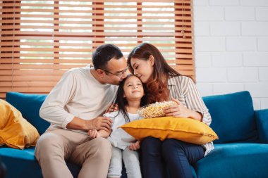 Ebeveynlerden oluşan Asyalı bir aile, evde oturma odasındaki kanepede patlamış mısır yiyen mutlu bir kız ya da televizyon izleyen bir film. Rahatlatıcı mutluluğun tadını çıkar.