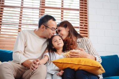 Ebeveynlerden oluşan Asyalı bir aile, evde oturma odasındaki kanepede patlamış mısır yiyen mutlu bir kız ya da televizyon izleyen bir film. Rahatlatıcı mutluluğun tadını çıkar.