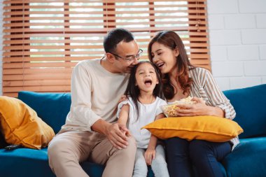 Ebeveynlerden oluşan Asyalı bir aile, evde oturma odasındaki kanepede patlamış mısır yiyen mutlu bir kız ya da televizyon izleyen bir film. Rahatlatıcı mutluluğun tadını çıkar.