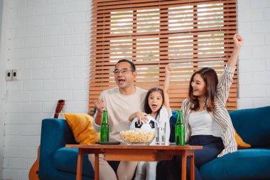 Kızıyla birlikte Asya Ailesi maç izlerken heyecanla evdeki oturma odasındaki kanepede patlamış mısır yiyor. Rahatlatıcı mutluluğun tadını çıkar.
