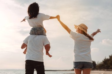 Mutlu Asyalı aile deniz sahilinin tadını çıkarıyor. Baba, anne ve kız, yaz tatilinde okyanus sahilinde plaj oynarken eğleniyorlar. Tatil hayatı konsepti olan mutlu bir aile..