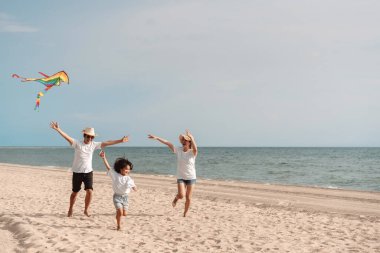 Mutlu Asyalı aile deniz sahilinin tadını çıkarıyor. Baba, anne ve kız, yaz tatilinde okyanus sahilinde plaj oynarken eğleniyorlar. Tatil hayatı konsepti olan mutlu bir aile..