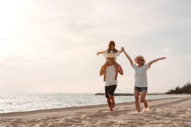 Mutlu Asyalı aile deniz sahilinin tadını çıkarıyor. Baba, anne ve kız, yaz tatilinde okyanus sahilinde plaj oynarken eğleniyorlar. Tatil hayatı konsepti olan mutlu bir aile..