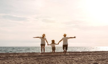 Mutlu Asyalı aile deniz sahilinin tadını çıkarıyor. Baba, anne ve kız, yaz tatilinde okyanus sahilinde plaj oynarken eğleniyorlar. Tatil hayatı konsepti olan mutlu bir aile..