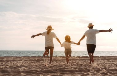 Mutlu Asyalı aile deniz sahilinin tadını çıkarıyor. Baba, anne ve kız, yaz tatilinde okyanus sahilinde plaj oynarken eğleniyorlar. Tatil hayatı konsepti olan mutlu bir aile..