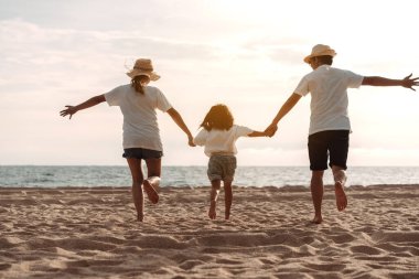 Mutlu Asyalı aile deniz sahilinin tadını çıkarıyor. Baba, anne ve kız, yaz tatilinde okyanus sahilinde plaj oynarken eğleniyorlar. Tatil hayatı konsepti olan mutlu bir aile..