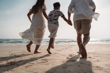 Mutlu Asyalı aile tatilde plajda birlikte eğleniyor. Aile deniz sahilinde gün batımının tadını çıkarırken el ele tutuşuyor. Mutlu aile seyahatleri, tatiller..