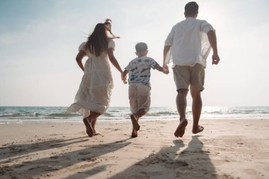 Mutlu Asyalı aile tatilde plajda birlikte eğleniyor. Aile deniz sahilinde gün batımının tadını çıkarırken el ele tutuşuyor. Mutlu aile seyahatleri, tatiller..