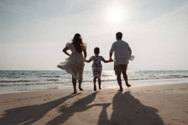 Mutlu Asyalı aile tatilde plajda birlikte eğleniyor. Aile deniz sahilinde gün batımının tadını çıkarırken el ele tutuşuyor. Mutlu aile seyahatleri, tatiller..