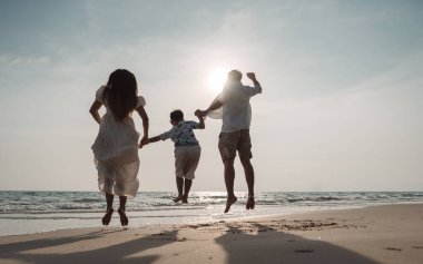 Mutlu Asyalı aile tatilde plajda birlikte eğleniyor. Aile deniz sahilinde gün batımının tadını çıkarırken el ele tutuşuyor. Mutlu aile seyahatleri, tatiller..