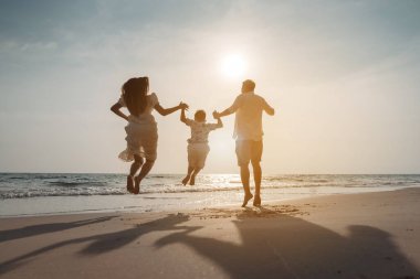 Mutlu Asyalı aile tatilde plajda birlikte eğleniyor. Aile deniz sahilinde gün batımının tadını çıkarırken el ele tutuşuyor. Mutlu aile seyahatleri, tatiller..
