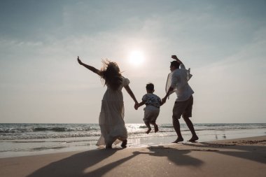 Mutlu Asyalı aile tatilde plajda birlikte eğleniyor. Aile deniz sahilinde gün batımının tadını çıkarırken el ele tutuşuyor. Mutlu aile seyahatleri, tatiller..
