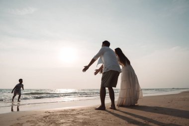Mutlu Asyalı aile tatilde plajda birlikte eğleniyor. Ailenin silueti deniz sahilinde gün batımının tadını çıkarıyor. Mutlu aile seyahatleri, tatiller..