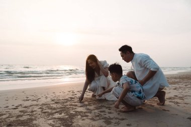 Mutlu Asyalı aile tatilde plajda birlikte eğleniyor. Ailenin silueti deniz sahilinde gün batımının tadını çıkarıyor. Mutlu aile seyahatleri, tatiller..