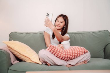 Asyalı Kadın Kanepe Selfie Smile Smartphone Salon İçi Koltuk Bağlantısı, Mutlu Genç Bayan Evde Rahatlıyor, Keyifli Video Görüşmesinin ve Oturma Odasında Sevgi ve Eğlencenin Anlarını Çekiyor