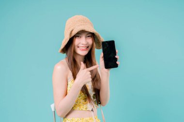 Online bilet rezervasyonu ve alımı için akıllı telefonu kullanan Asyalı Kadın, stüdyonun arka planında cep telefonu tutan genç kadın yaz tatili kavramı.