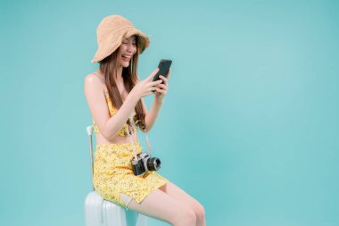 Online bilet rezervasyonu ve alımı için akıllı telefonu kullanan Asyalı Kadın, stüdyonun arka planında cep telefonu tutan genç kadın yaz tatili kavramı.