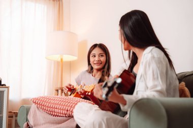Asya Kadın Müzik Gitarı Birlikte Çalıyor Salonda Genç Gençler Oturma Odası, Arkadaşların Neşeli Toplantısı Müzik Paylaşımı, Gülüşmeler ve Evde Gitar Çalarak Rahatlama