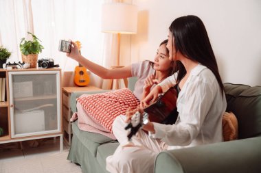 Asya Kadın Müzik Gitarı Birlikte Çalıyor Salonda Genç Gençler Oturma Odası, Arkadaşların Neşeli Toplantısı Müzik Paylaşımı, Gülüşmeler ve Evde Gitar Çalarak Rahatlama