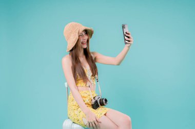 Online bilet rezervasyonu ve alımı için akıllı telefonu kullanan Asyalı Kadın, stüdyonun arka planında cep telefonu tutan genç kadın yaz tatili kavramı.