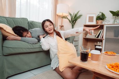 Asyalı Kadın Atıştırmalığı Yaşam Tarzı Oturma Odası Keyif Filmi, Televizyon izlerken İki Genç Yetişkin Kahkaha ve Atıştırma, Evde Arkadaşlık ve Gevşemeyi Kucaklaşma