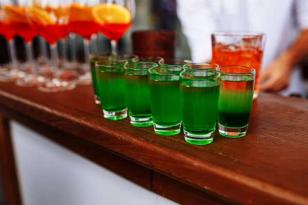 stock image Drinks for St. Patrick's Day party. Good luck leprechaun shot cocktail. Green strong drink in a shot glass. Glasses of Aperol Spritz and Shots or Shooters on wooden bar counter in a restaurant, pub