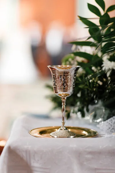 golden chalice with drawings on it for drinking wine for communion on the golden plate in church. Greens on background. copy space. selective focus.