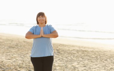 Yoga and meditation of mature woman practicing breath exercises on the sea beach on sunrise in the morning. Body mind and spirit, mindfulness concept. Enlightenment and healthy lifestyle