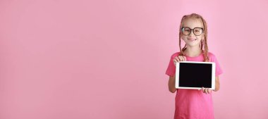 Elinde tabletle pembe arka planda gülümseyen komik kız çocuğu. Gözlüklü beyaz çocuk boş ekran gösteriyor ve kameraya bakıyor. Reklamlar boş. Gözbebeği ürünü tanıtıyor
