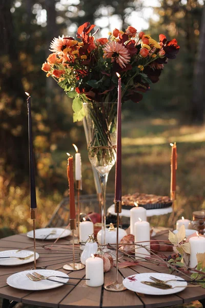 公園で居心地の良い秋のピクニック 白いプレート カトラリー カラフルな野の花とガラスの花瓶 自家製のリンゴパイ メープルの葉 木製のテーブルの上に燃えるろうそく屋外でテーブルの設定を閉じます — ストック写真