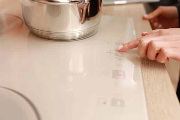 女性的手打开电杆特写 手指按下现代白色感应炊具上的传感器按钮 厨房炉顶面板上的金属铁锅 烹调表面的方式 家用设备 — 图库照片
