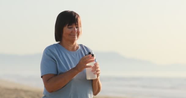 Uśmiechnięta Kobieta Pije Wodę Plastikowej Butelki Nad Morzem Słoneczny Letni — Wideo stockowe