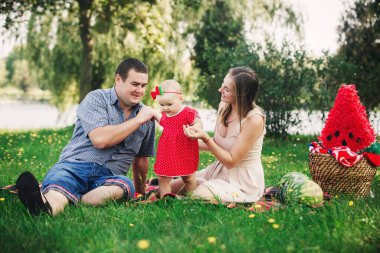 Aile piknikte. Anne, baba ve küçük kız parkta battaniyenin üzerinde oturuyorlar. Yaz tatili kavramı. Anneler günü, babalar günü, bebekler günü. Birlikte vakit geçirmek.