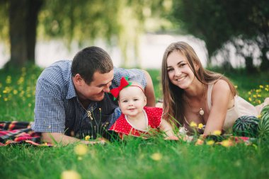 Aile piknikte. Anne, baba ve küçük kız parkta battaniyenin üzerinde oturuyorlar. Yaz tatili kavramı. Anneler günü, babalar günü, bebekler günü. Birlikte vakit geçirmek.