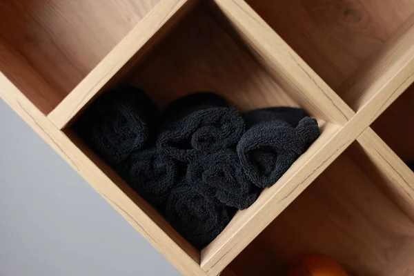 Stack of many clean black towels on two wooden shelves on white wall background for customer of spa, barbershop, or gym, beauty salon and tourist take it to shower in the bath room