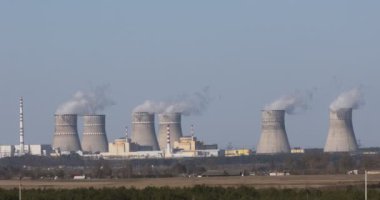 Nükleer santral manzarası. Mavi gökyüzünün altında, nükleer santralin, elektrik hatlarının ve ormanın tüten bacalarının görüntüsü.