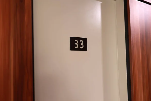 stock image Hotel room 33 number mounted on a white wall. White number on black board by wooden doors in corridor hall.