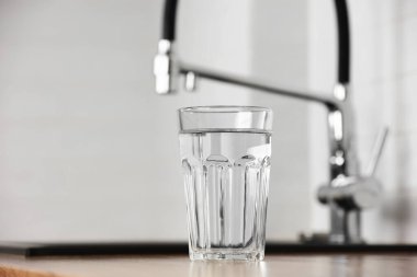 Mutfağın içindeki ahşap masada şeffaf temiz filtreli su bardağı. Mutfak lavabosunun osmoz sistemiyle arıtılmış suyu olan musluk..