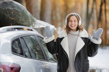 Gülümseyen kadın, arabanın yanında, çatıda ışıklandırılmış Noel ağacı olan kulaklıkla xmas müziği dinliyor. Yeni yıl hazırlığı kavramı. Kış tatilinde peri masalı ve şenlik havası..
