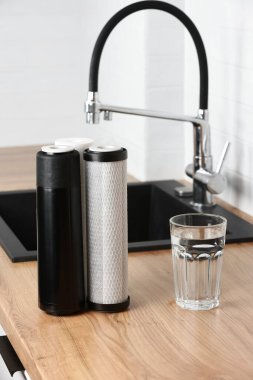 Bir bardak temiz su ve mutfak içlerindeki ahşap masa üzerindeki filtre kartuşları. Ters osmoz su arıtma sisteminin kurulumu. Konsept Ev filtreleme sistemi