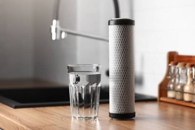 Bir bardak temiz su ve karbon filtre kartuş mutfak içinde ahşap masa üzerinde. Ters osmoz su arıtma sisteminin kurulumu. Konsept Ev filtreleme sistemi