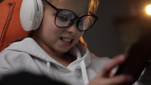 소녀는 소파에 디지털 태블릿 장치로 집에서 게임을 헤드폰 안경을 정서적 — 비디오