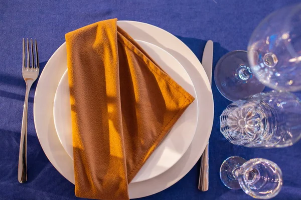 Festive Christmas, wedding, birthday table setting with blue tablecloth, orange napkin cutlery, white plates, glasses for wine, water and strong alcoholic beverages. Flat lay.