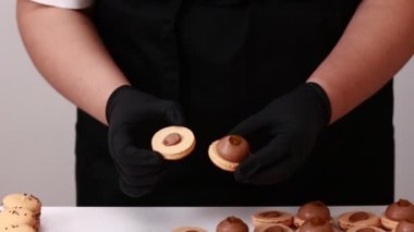 Process of making macarons macaroons, french dessert. chef hands in black gloves are assembling, connecting of two halves with chocolate stuffing at pastry shop. cooking, food and baking concept