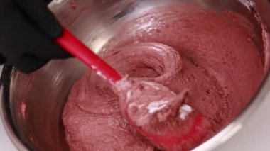 The pastry chef mixes silicone spatula the brown dough for the French desert macaron or macaroon in a stainless steel bowl, the process of preparing the cakes. Concept of confectionery or pastry shop.
